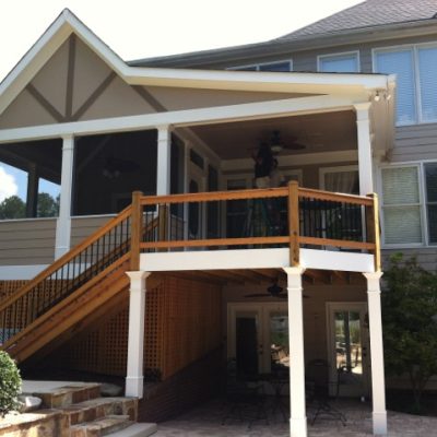A two-story house featuring a screened-in balcony and stairs leading to a patio, masterfully enhanced by Painting Plus. The patio hosts a table with chairs underneath, inviting relaxation amidst beautifully curated surroundings.