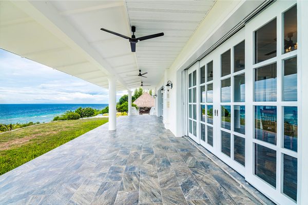 patio-door-and-window-installation Spacious veranda with tile flooring by Painting Plus, featuring white doors and ceiling fans, offering a stunning ocean view.