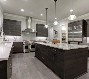 Modern kitchen with dark wood cabinets, stainless steel appliances, a large granite island, pendant lighting, light wood flooring, and interior paint colors that enhance the sleek design.