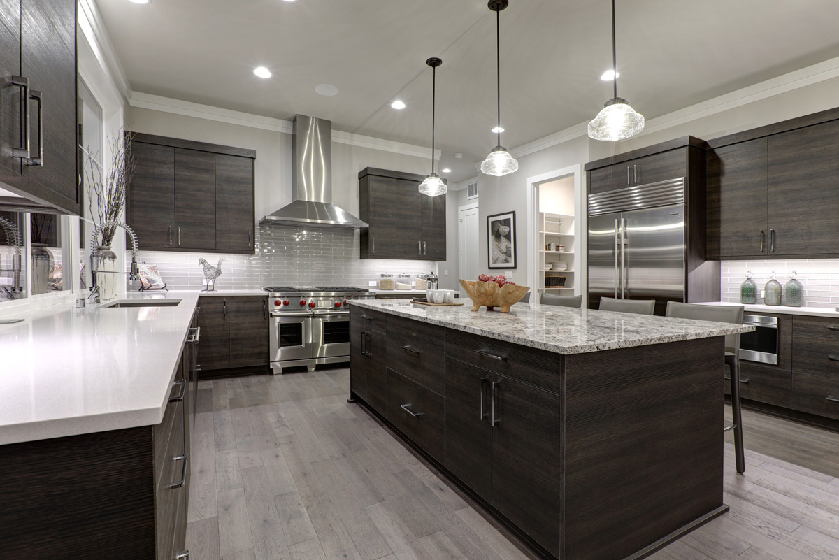 Modern kitchen with dark wood cabinets, stainless steel appliances, a large granite island, pendant lighting, light wood flooring, and interior paint colors that enhance the sleek design.